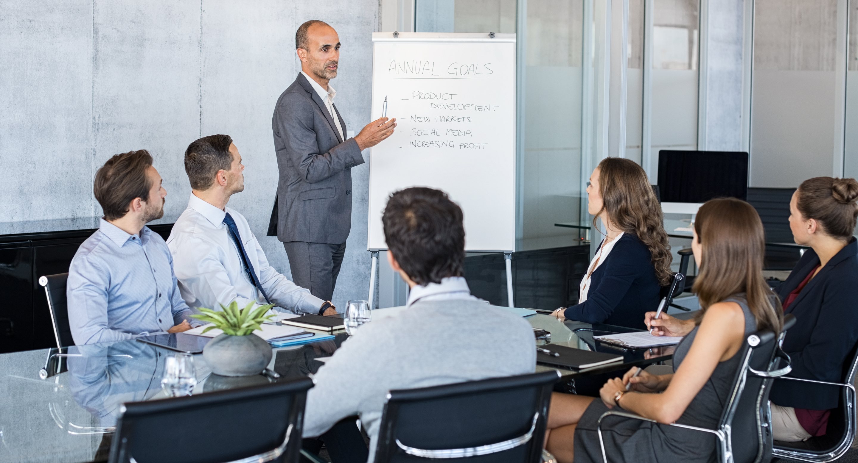 Executive presenting annual goals on a flip chart to his team in a boardroom